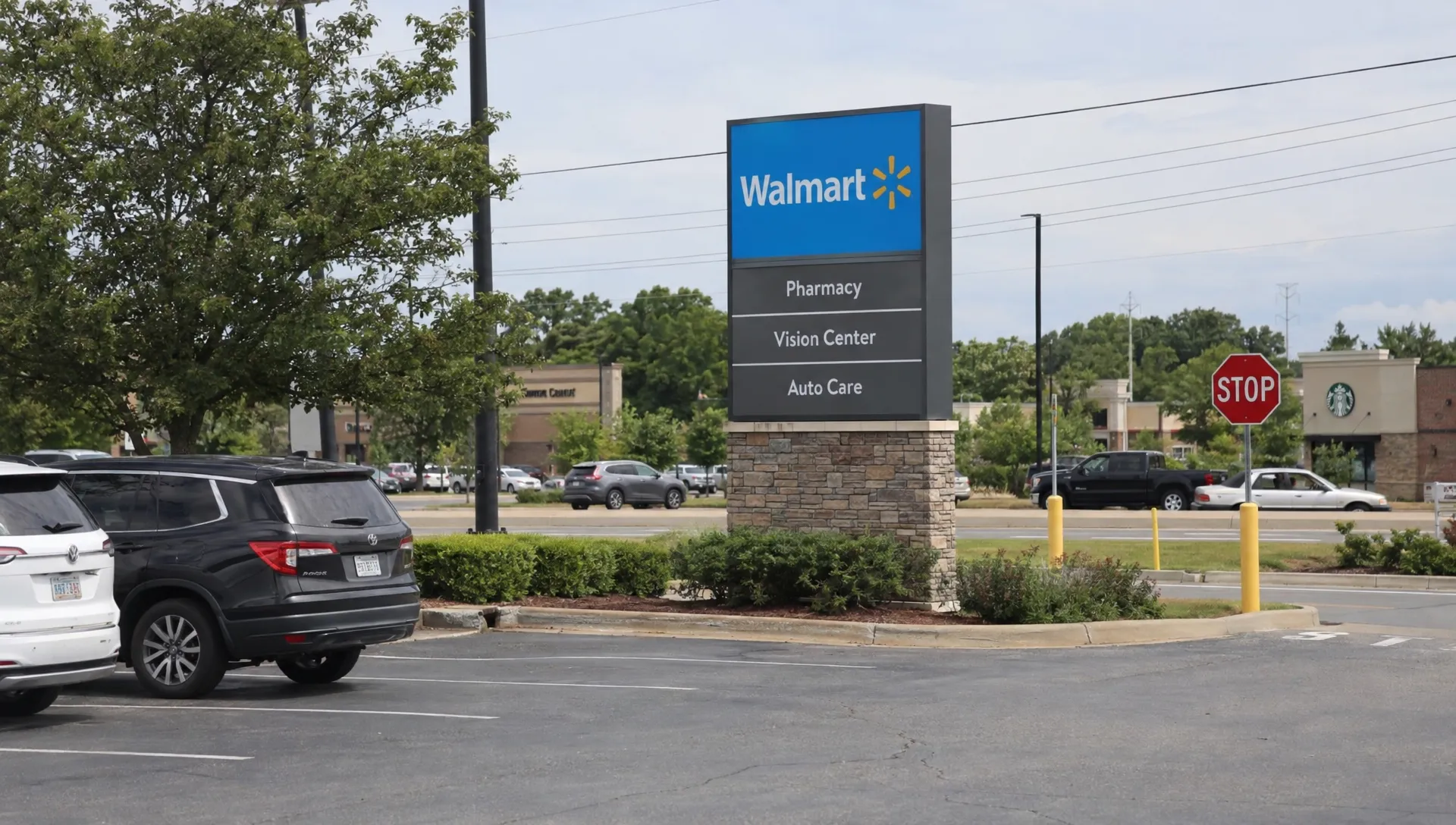 A pylon sign displays a business name above parked cars beside the visible driveway to a set-back commercial property.