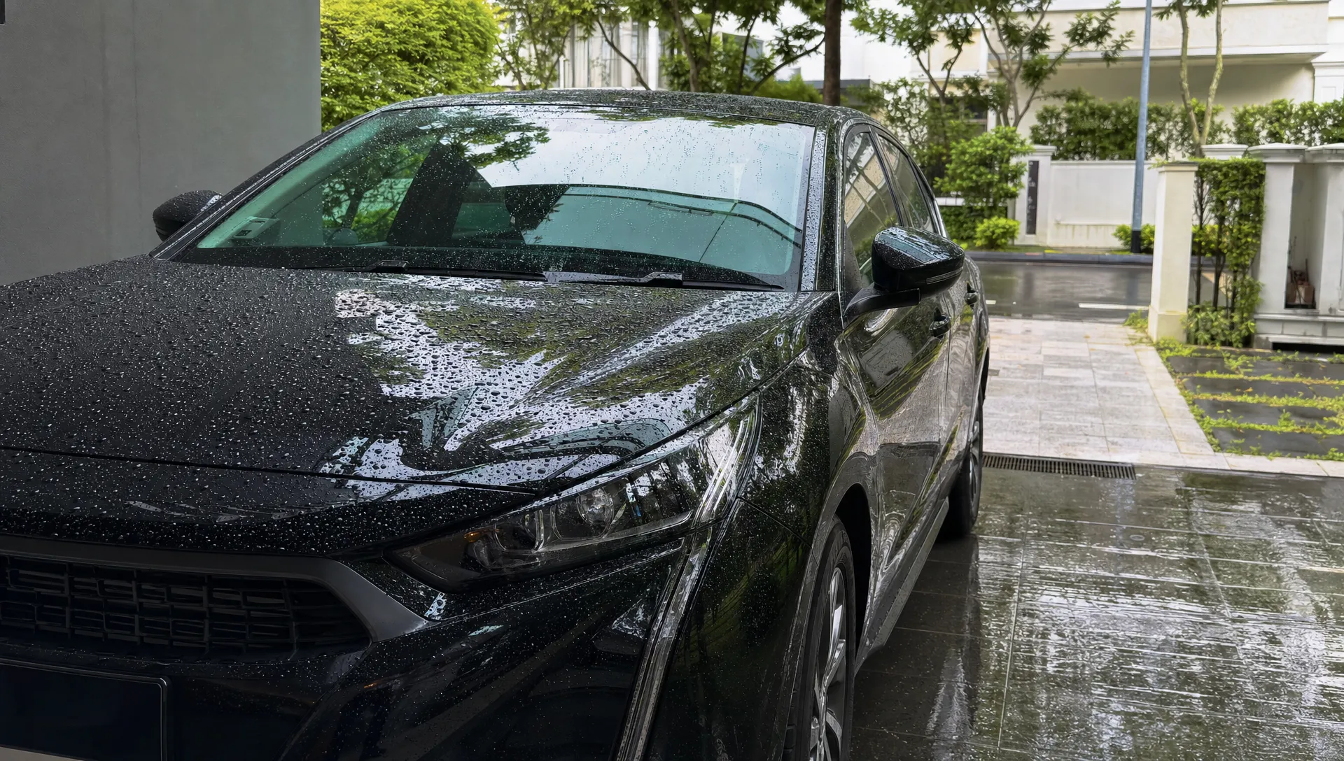 A glossy dark-coloured car sits in a Singapore driveway after rain, with tight water beads on the bonnet and reflections of nearby greenery.