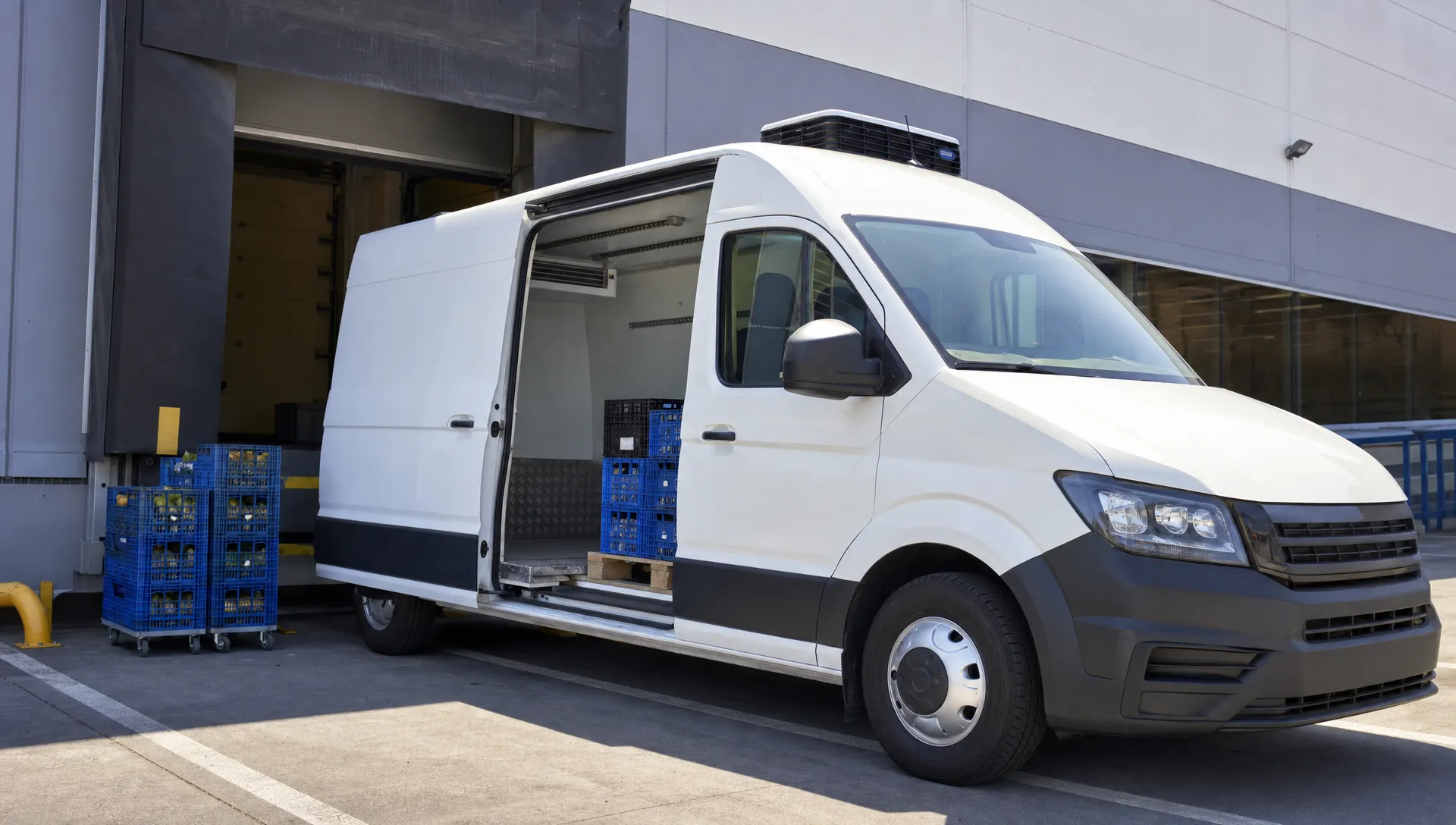 Een transporter koelwagen staat bij een laadplaats met open laadruimte, koelunit en kratten voor gekoelde bezorging.