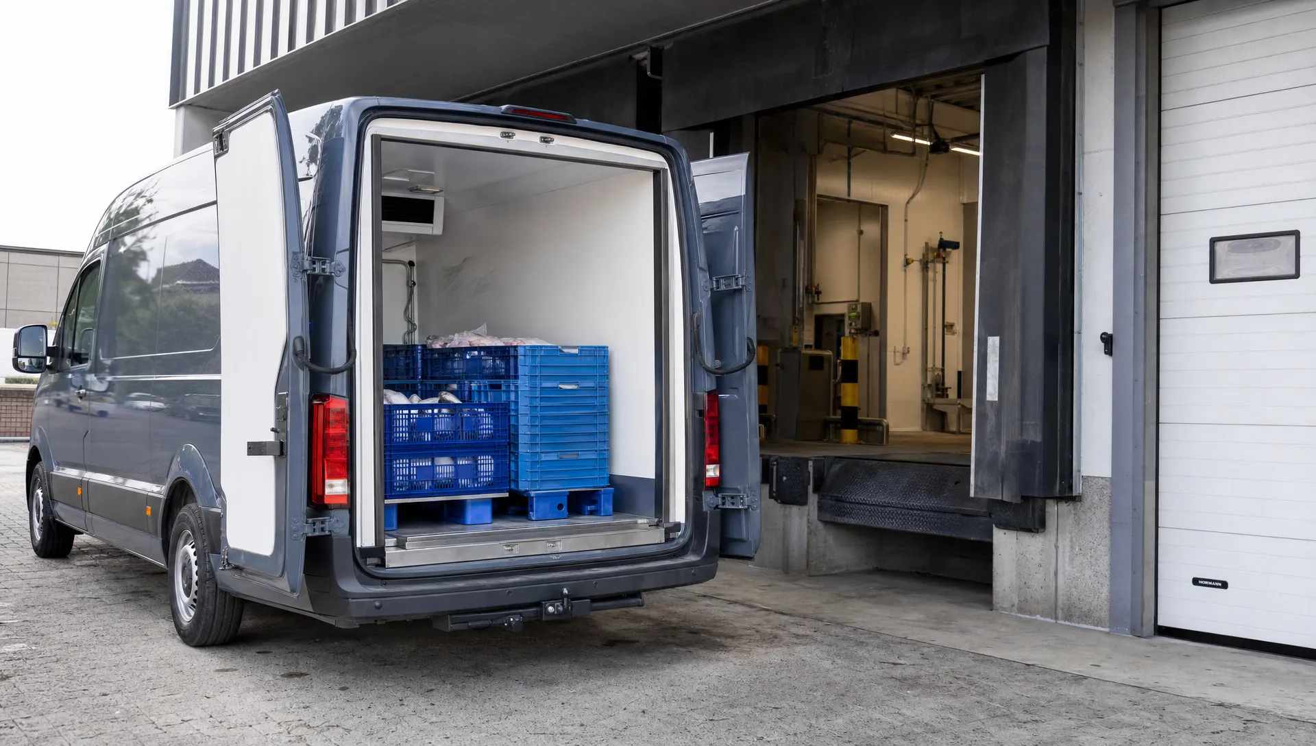 Een MAN bestelwagen staat met geopende achterdeuren bij een laadperron, terwijl geïsoleerde wanden en kratten met gekoelde lading zichtbaar zijn.